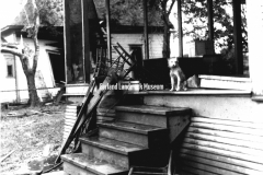 1927 Garland Tornado Damage.  House with dog sitting on front porch. Marilyn and Marta Lyle look over the pleasure boat, "Bonnie Barge"