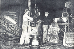 Cotton sack and wagon, two men in picture. Two employees of Watson Seed Company weighing and sacking cotton seed at the Watson plant on Walnut Street. circa 1930's.