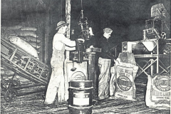 Cotton sack and wagon, two men in picture. Two employees of Watson Seed Company weighing and sacking cotton seed at the Watson plant on Walnut Street. circa 1930's.