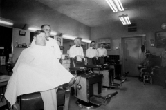 Owl Barbershop, mid-1950's.  Faced south on the lower floor of the State National Bank building..  Bob Walker (McKnight Drugs - in chair). (front-rear) George Brannon (barber), Fred L. Gray (barber), Ralph Johnson (barber), Joe A. Smith (barber), man known only as the One-legged Shoeshine Boy.