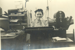 Helen Law Manzer at typewriter with mimeograph machine behind her.
