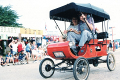 1901 Oldmobile automobile with fringed cover being driven in Star Spangled Fourth parade
