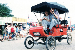 1901 Oldmobile automobile with fringed cover being driven in Star Spangled Fourth parade
