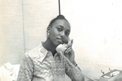 An African American woman on the phone. A sign behind her reads 'Productivity-Using tomorrow's ideas today'.