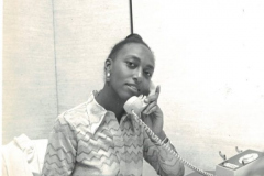 An African American woman on the phone. A sign behind her reads 'Productivity-Using tomorrow's ideas today'.
